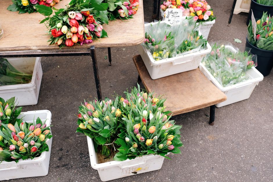 Multiple bouquets and arrangements of tulips in various stages of bloom, featuring pastel shades of pink, yellow, orange, and white, are displayed in white plastic crates and on small wooden stools. T