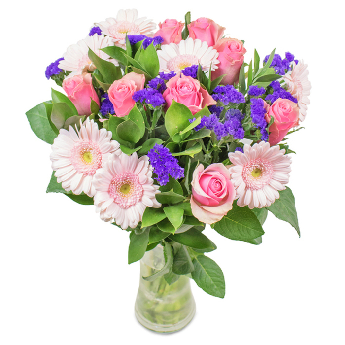 Presented by expert florists in Kidbrooke, this captivating bouquet immediately draws the eye with its refined blend of texture and tone. A prominent cluster of soft to medium pink roses-seven to nine in total-captivates with their spiral blooms, some still tightly furled, others just beginning to open, symbolizing unfolding affection. Pale pink gerbera daisies, five to seven in number, stretch their broad petals beside the roses, their lighter, almost powdery centers glowing gently. Scattered throughout, vibrant purple statice or limonium catches light and adds a playful burst of colour, offering a dynamic visual counterpoint. Deep green foliage encircles the arrangement, imparting freshness and vivacity reminiscent of Kidbrooke's abundant green spaces. Set in a simple, slender glass vase, the stems and water remain visible, emphasizing authenticity and just-picked beauty. The overall effect is uplifting and sophisticated, perfectly suited for celebrating a birthday, marking an anniversary, or sending affectionate wishes across Kidbrooke. Every detail-colour, shape, and presentation-has been selected to evoke joy, reinforce connection, and deliver a touch of classic elegance, highlighting the artistic commitment of local Kidbrooke florists.